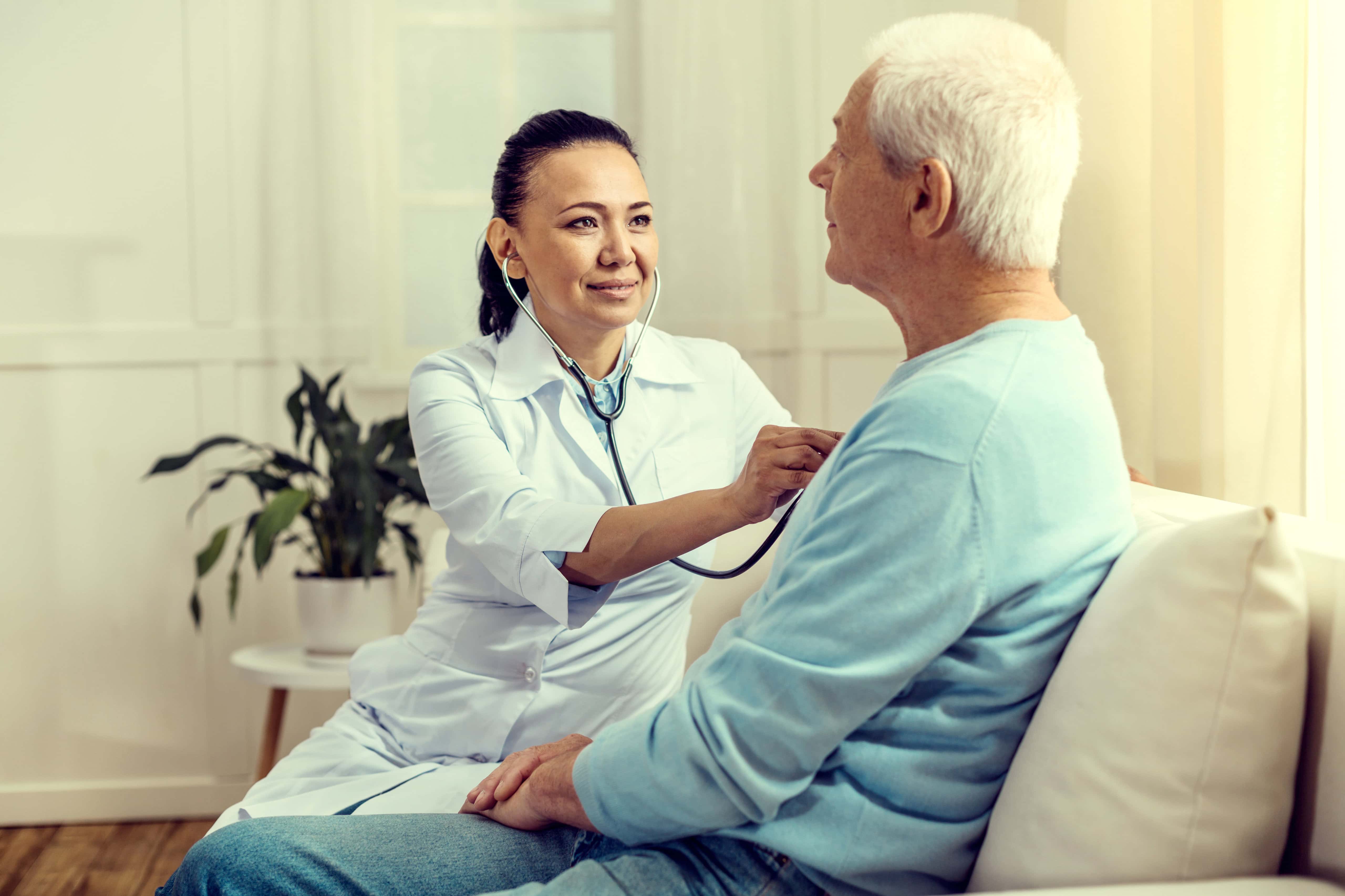 Smiling nurse listening to heart beating of retired patient